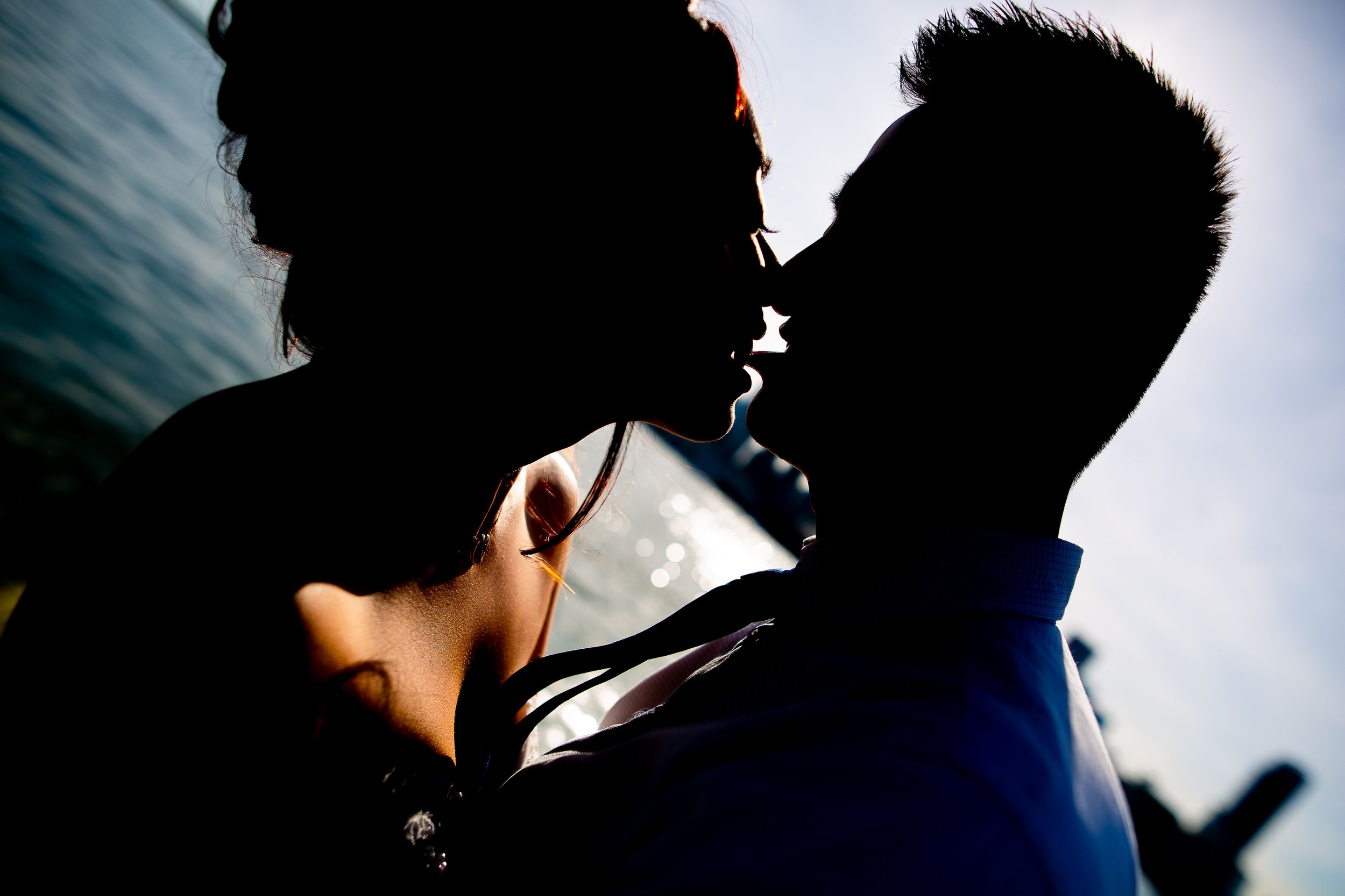 Silhouetted couple sharing an intimate moment against bright sky.