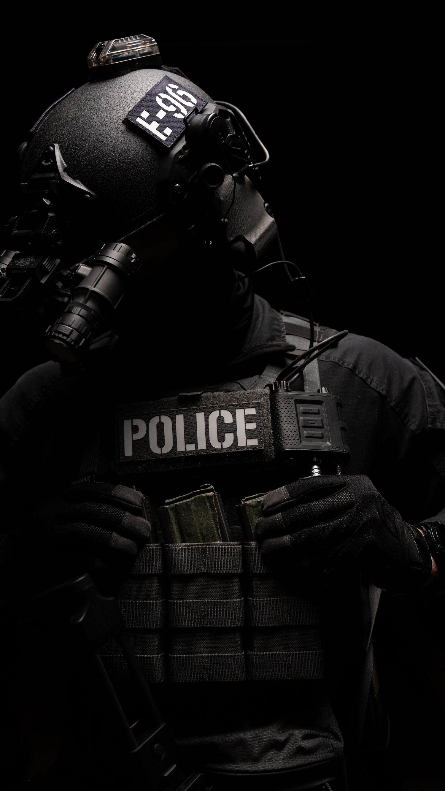 Dark dramatic image of tactical police officer in full riot gear with helmet and body armor against black background.