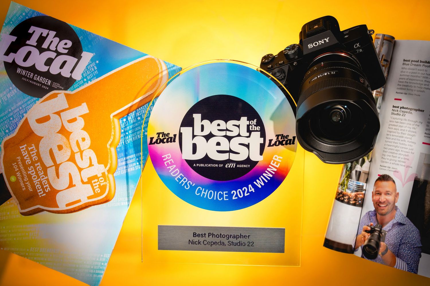 Photography awards and accolades shown with a DSLR camera against an orange background with blue circular emblems.