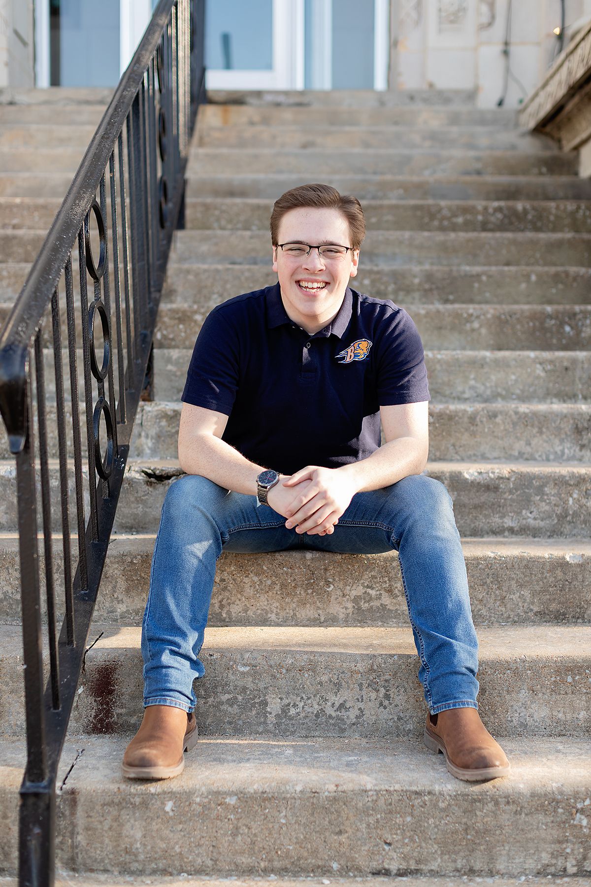 Senior picture by MegMc Photography of a male teen wearing his college choice shirt and smiling on the steps of old city hall in Jackson, TN