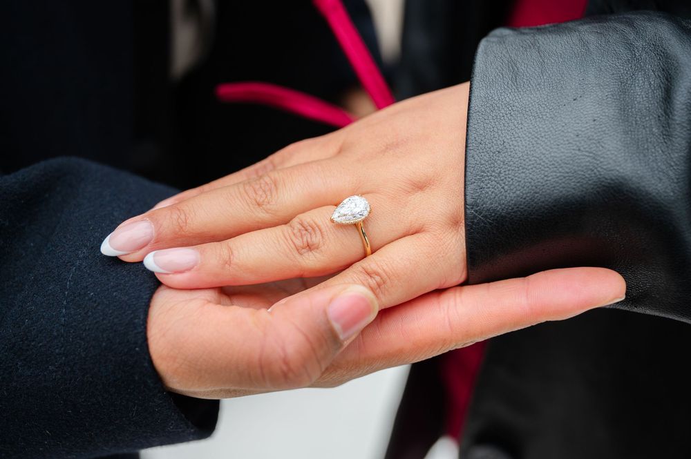 Close-up of an elegant pear-shaped diamond engagement ring being showcased on a hand with french manicured nails.
