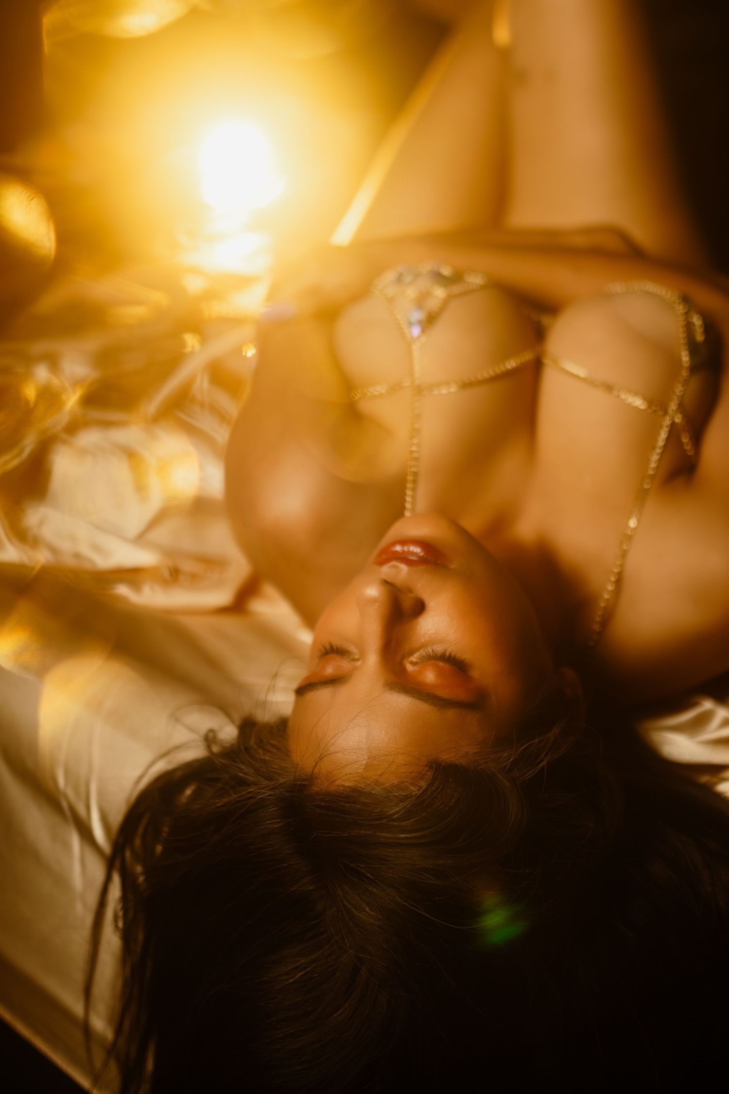 Artistic portrait in warm golden lighting with soft focus on jewelry details and satin textures at a Fort Worth, Texas boudoir studio.