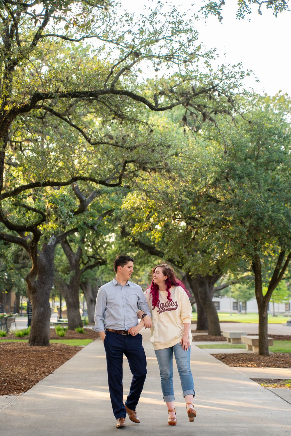 Couple walking together down a tree-lined pathway in a park on a sunny afternoon.
