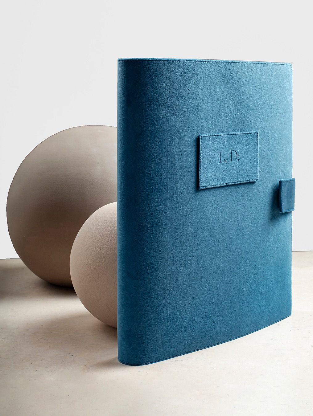 A minimalist blue leather notebook or journal with 'I.D.' embossed label sits beside neutral spherical objects.