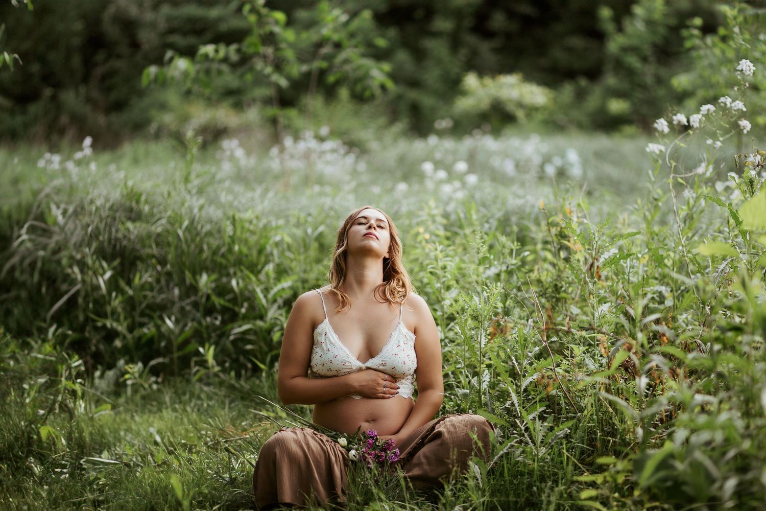 maternity photos in pittsburgh pennsylvania by ash coniglio photography, woman sits criss cross in a green field, holding belly, looking up