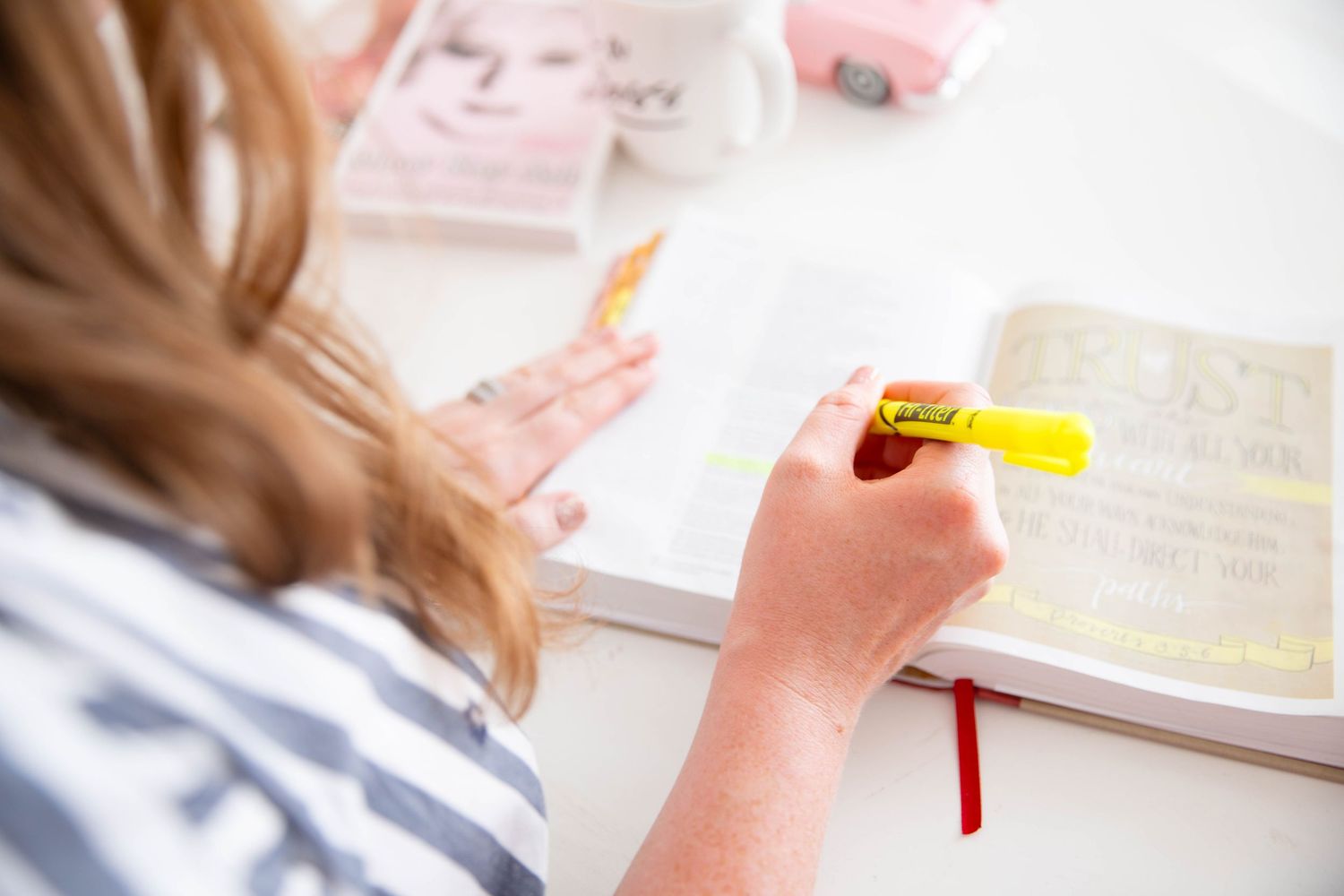 Student taking notes with a yellow highlighter pen studying at desk with textbooks and papers.