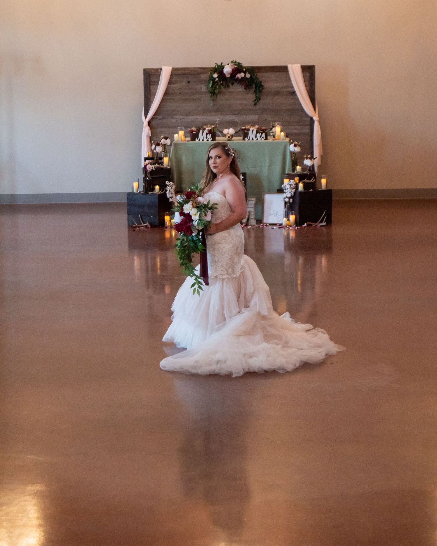 A bride in a flowing white wedding dress sits elegantly in a rustic event venue with warm lighting.
