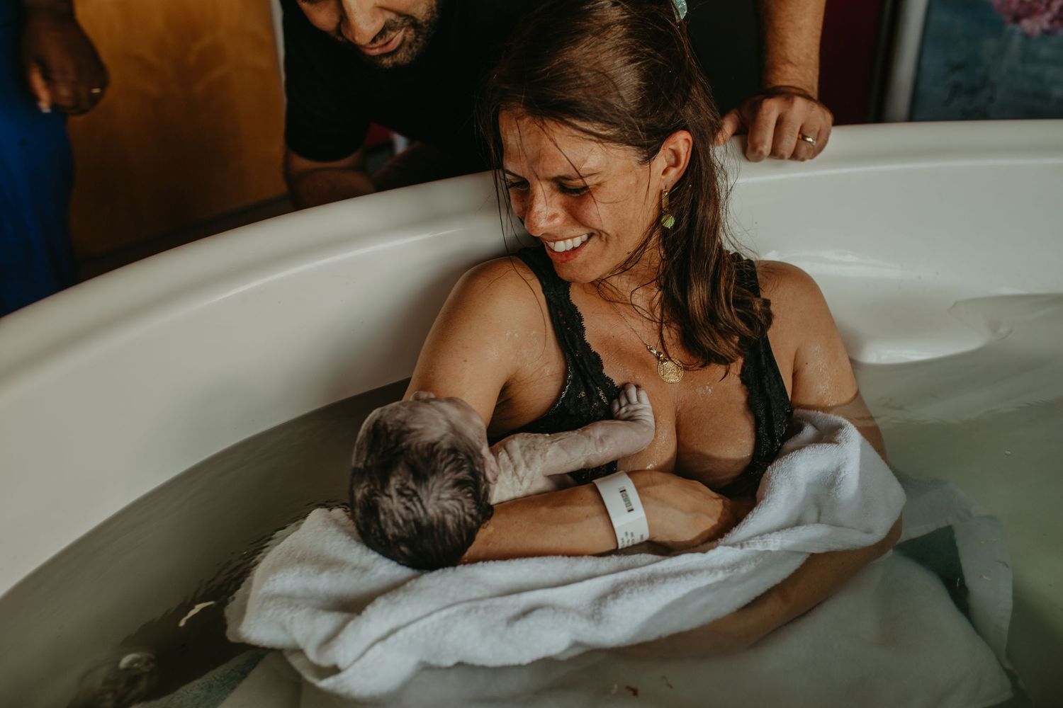 A mother breastfeeds her newborn baby in a birthing tub while in a maternity room.