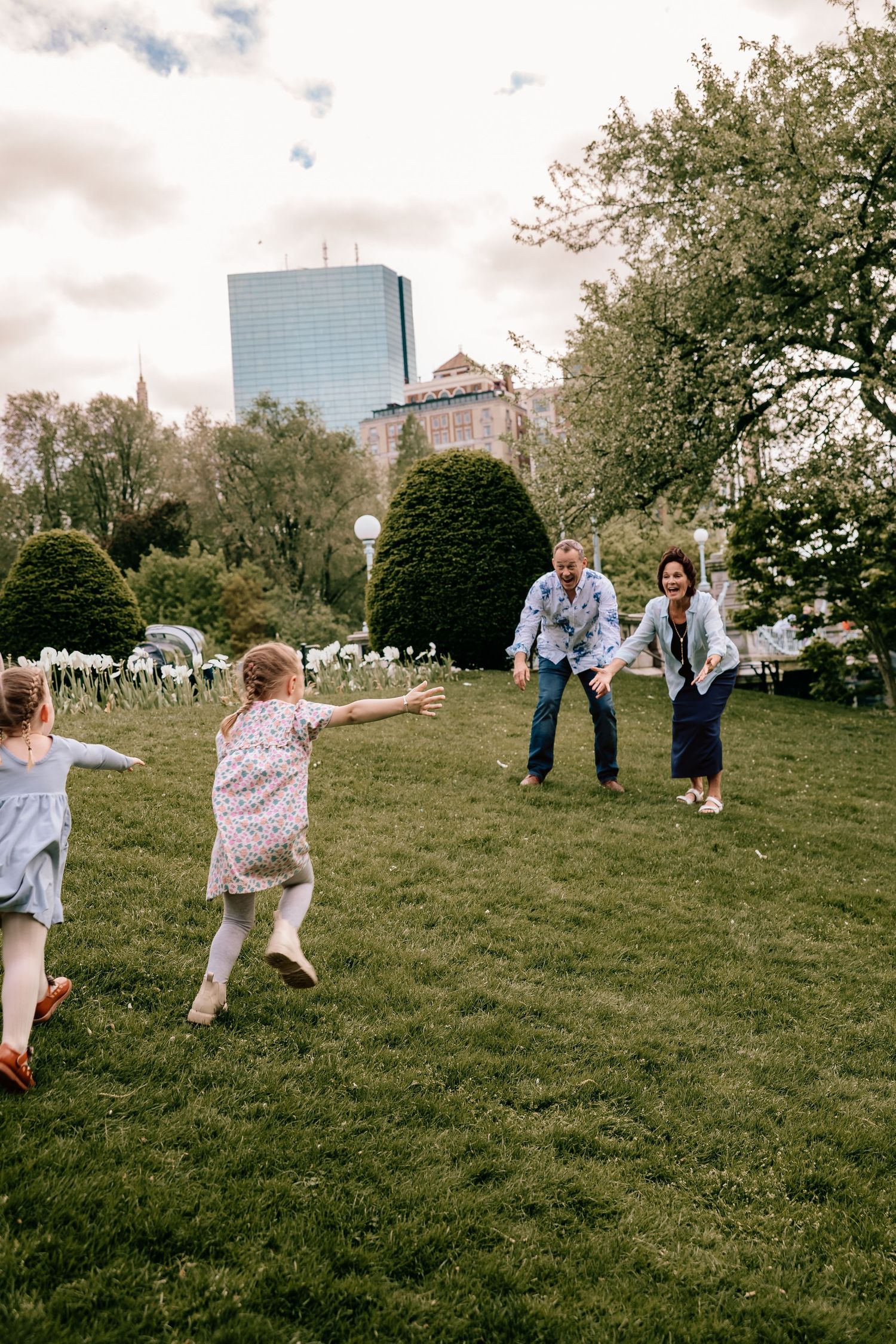 A group plays joyfully on a grassy slope with tall buildings visible in the background on an overcast day.