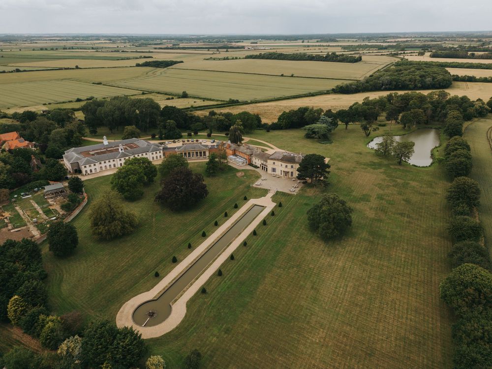 Aerial view of a grand estate with ornate gardens and sprawling green lawns in the countryside.