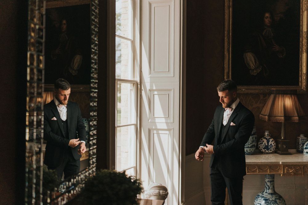 People in formal attire wait in an elegant room with ornate decor and period furniture.