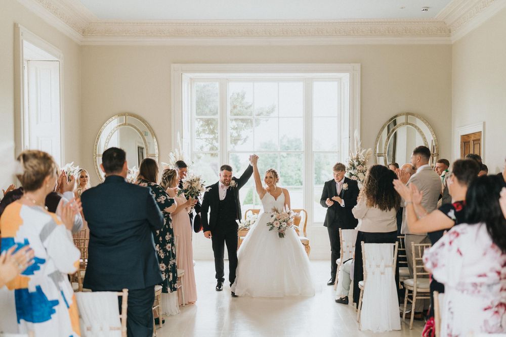 Wedding celebration in bright indoor venue with guests cheering for newlyweds entering after ceremony.
