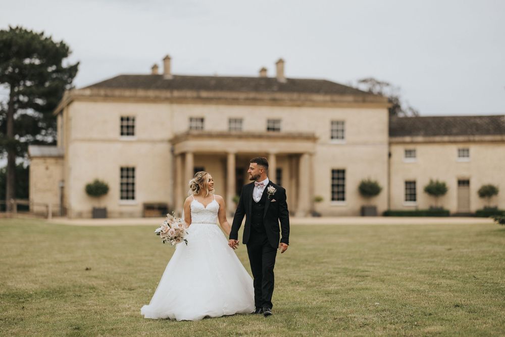 A couple poses in front of an elegant Georgian mansion with symmetrical architecture and landscaped grounds.