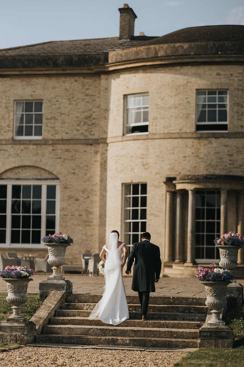 Wedding couple and guests posing on stone steps outside a grand historic mansion with curved architecture.