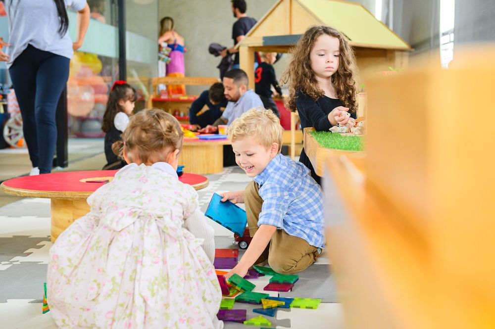Children playing with colorful toys and building blocks on floor mats in a daycare or learning center setting.