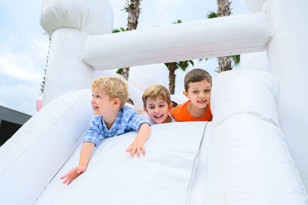 Three children having fun peeking out from the top of a white inflatable bounce house.