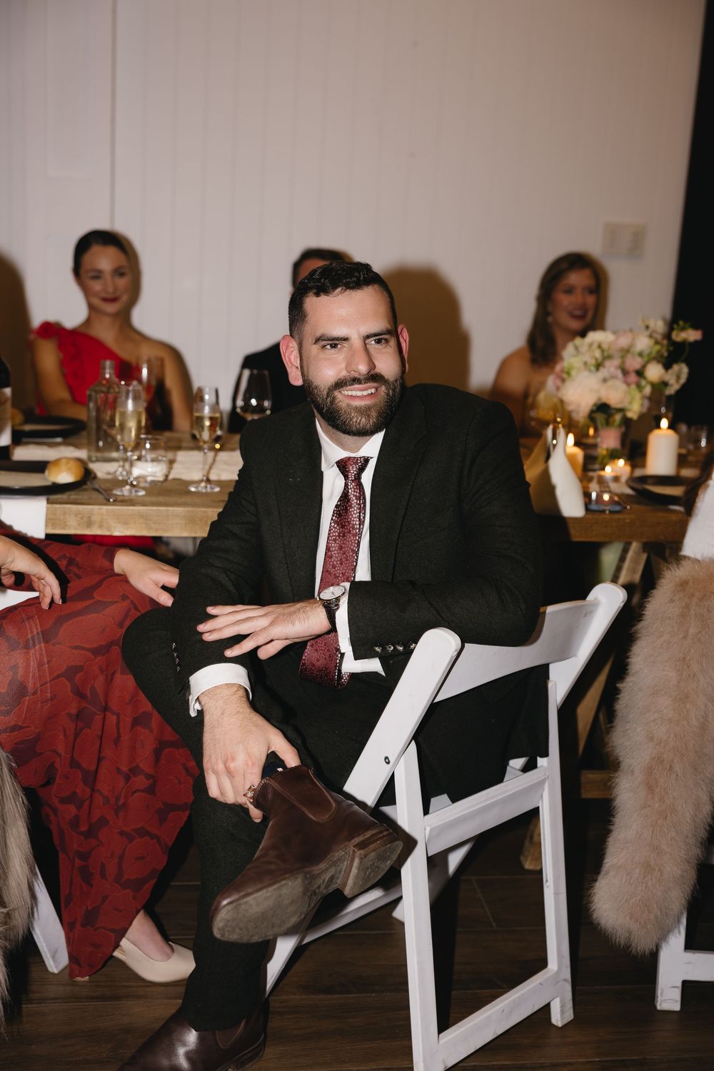 Formally dressed guest in dark suit and burgundy tie sits at an elegant wedding reception dinner table.