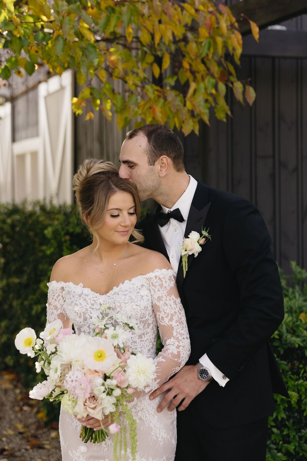 A romantic autumn wedding couple embraces underneath trees with golden yellow leaves during their portrait session.