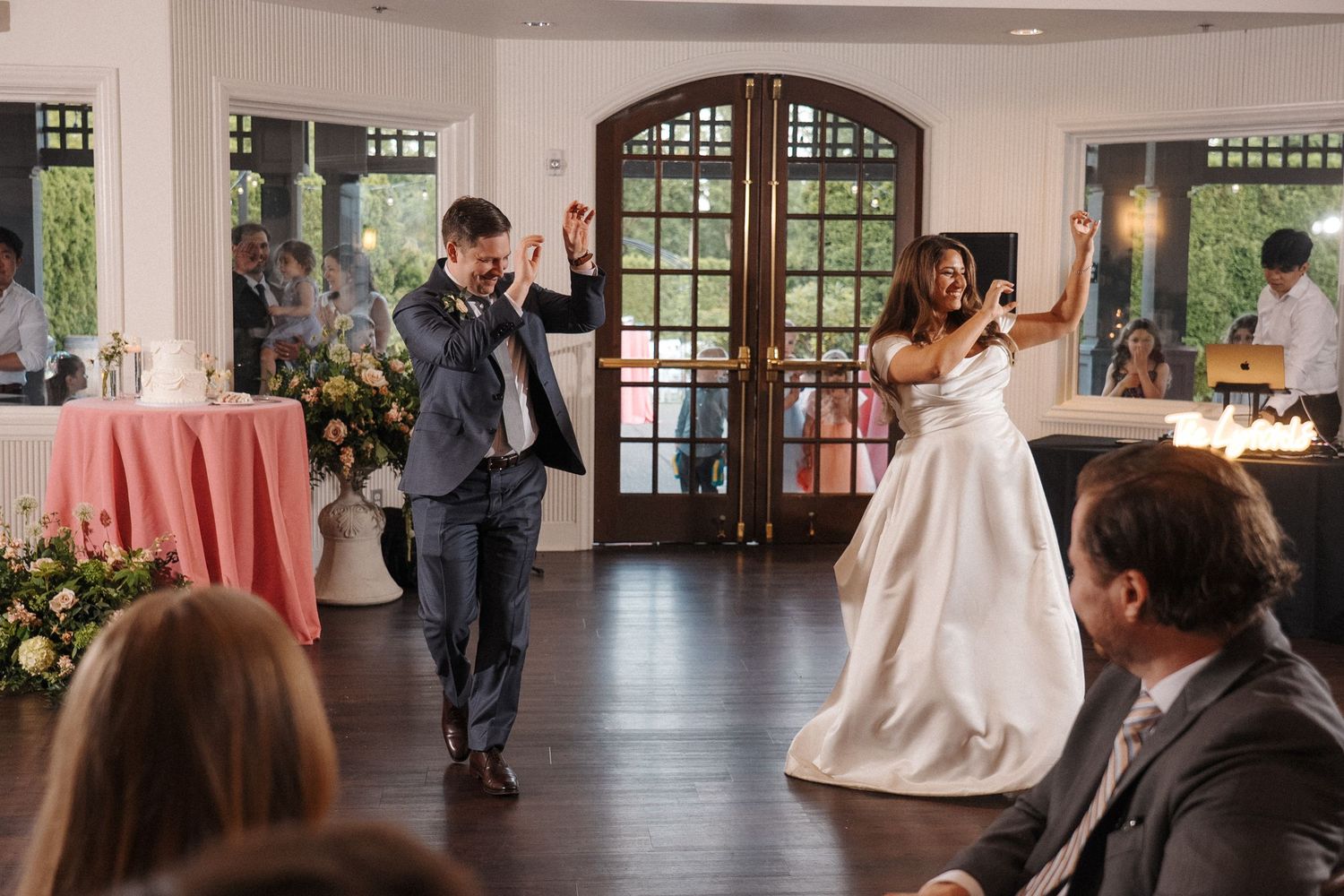 A wedding reception venue with large windows and round tables covered in light tablecloths.