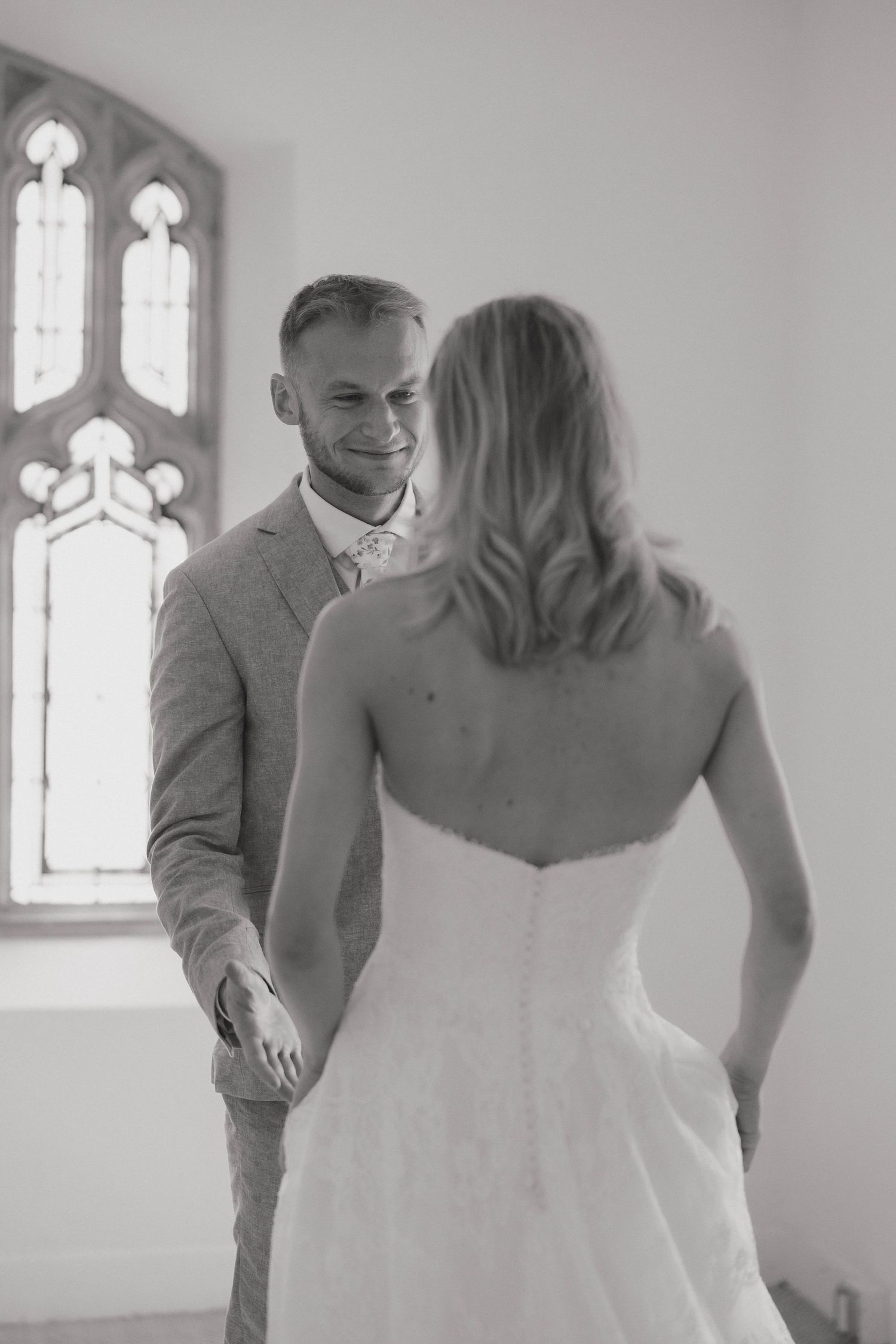 Black and white photo of a couple in wedding attire sharing an intimate moment in front of a church window.