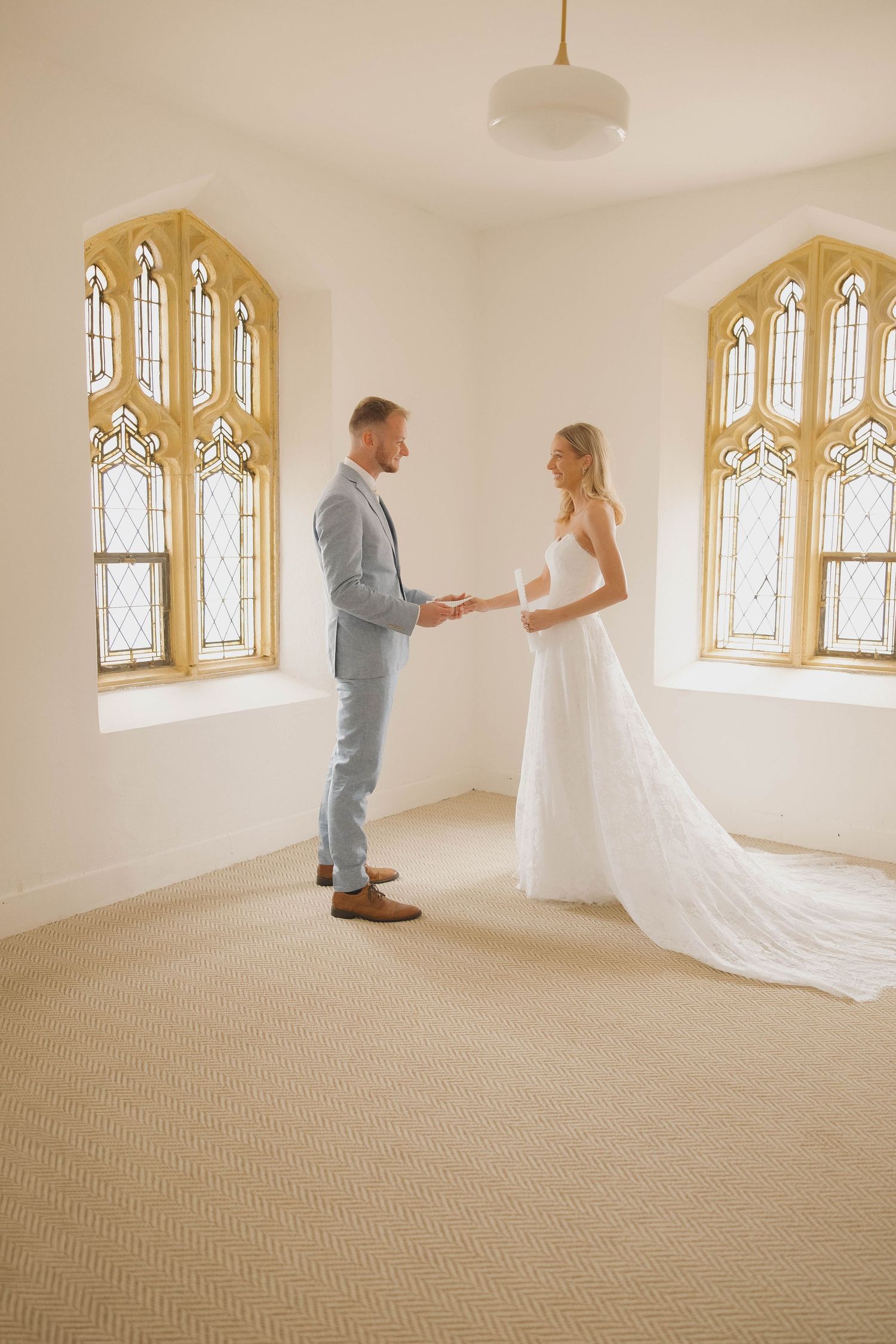 Wedding couple dances together in a light-filled chapel with Gothic arched windows and carpeted floor.