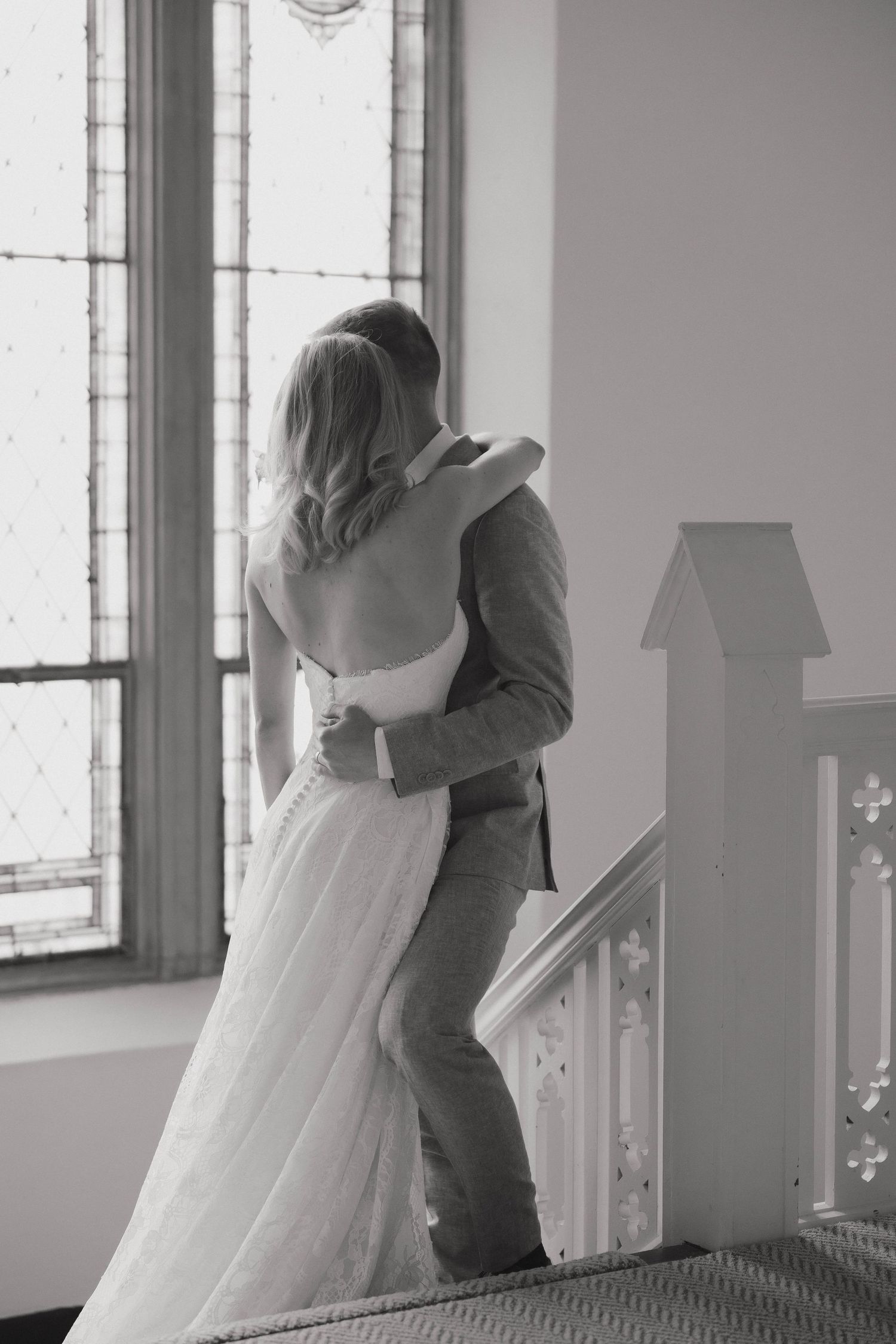 A romantic embrace between two people in a bright interior room with large windows.