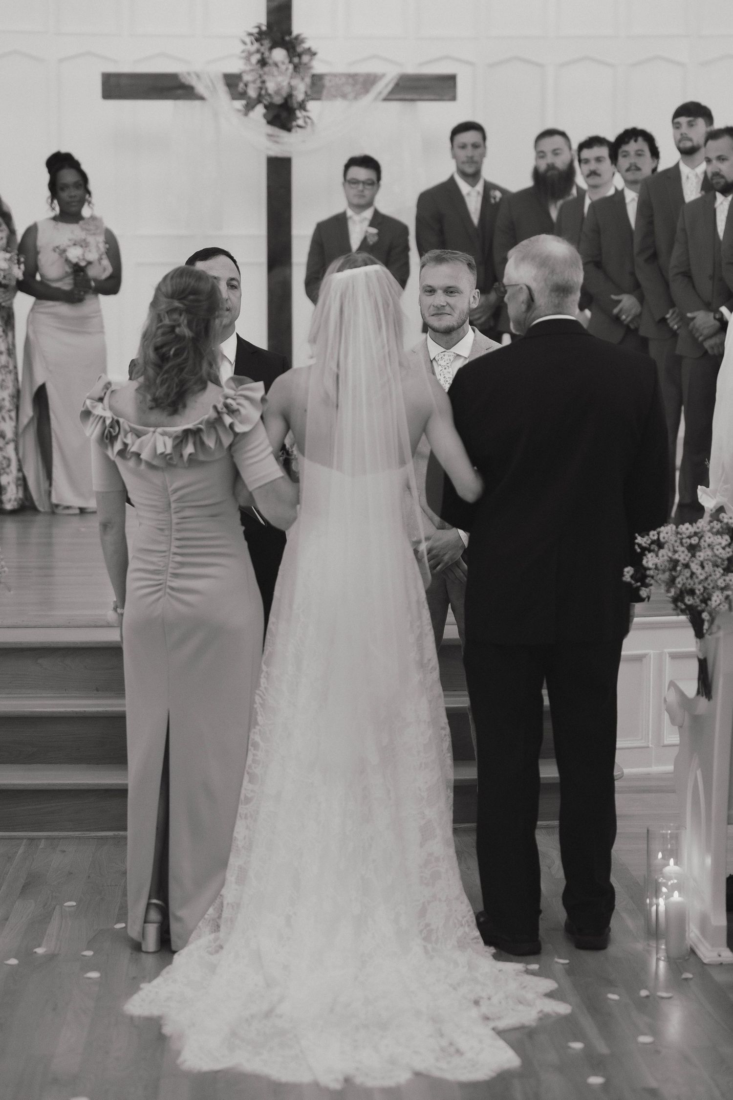 Black and white wedding ceremony photograph showing a small gathering by the altar under a wooden cross.