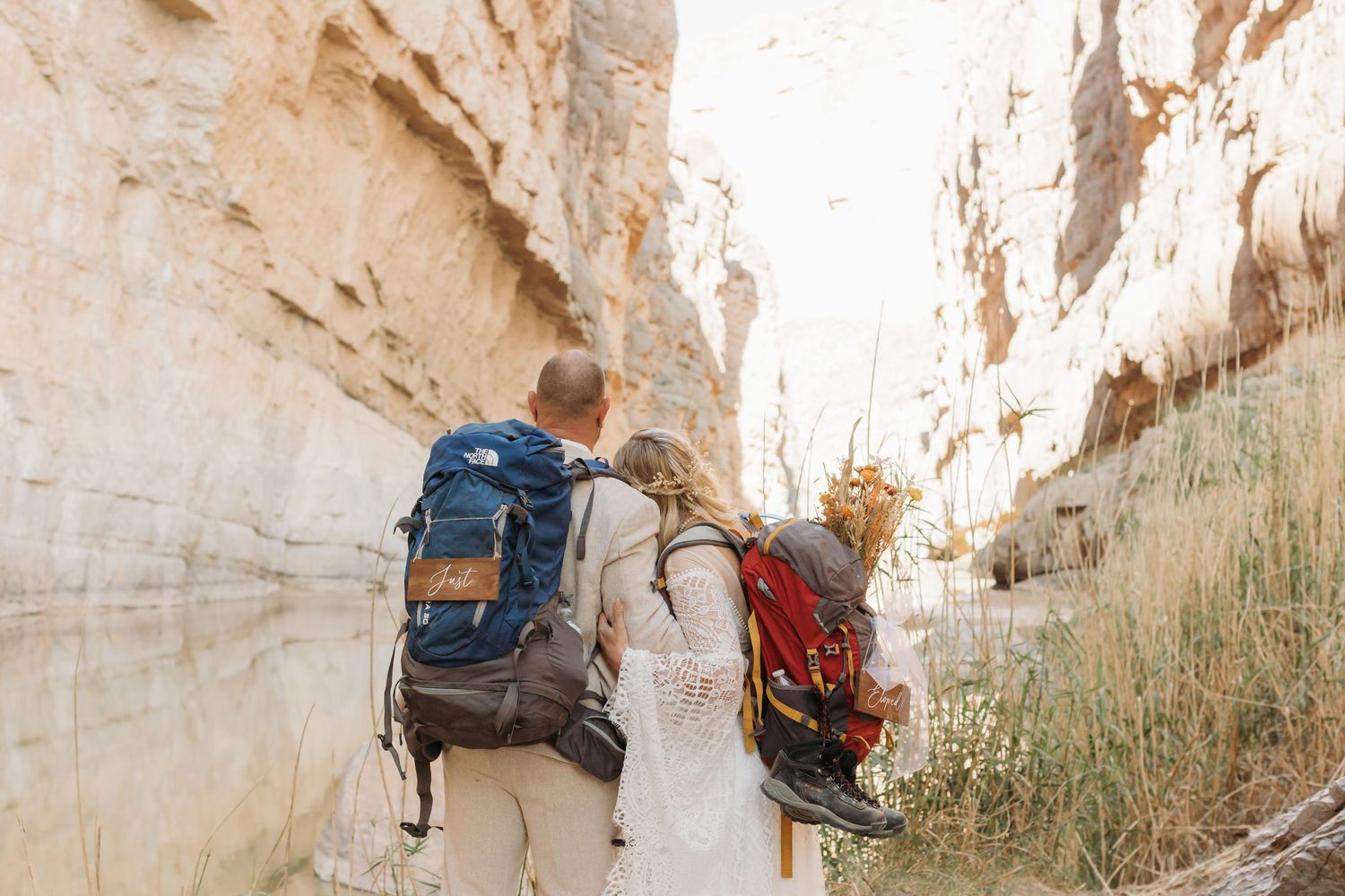 Hikers with backpacks walking through narrow desert canyon with towering sandstone walls.