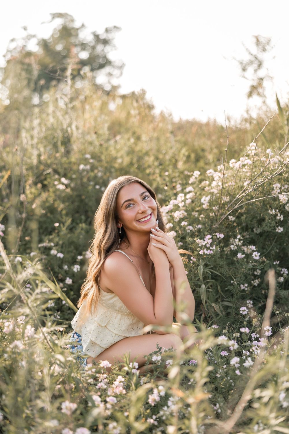Someone sits in a wildflower meadow wearing a yellow dress on a sunny summer day surrounded by white daisies.