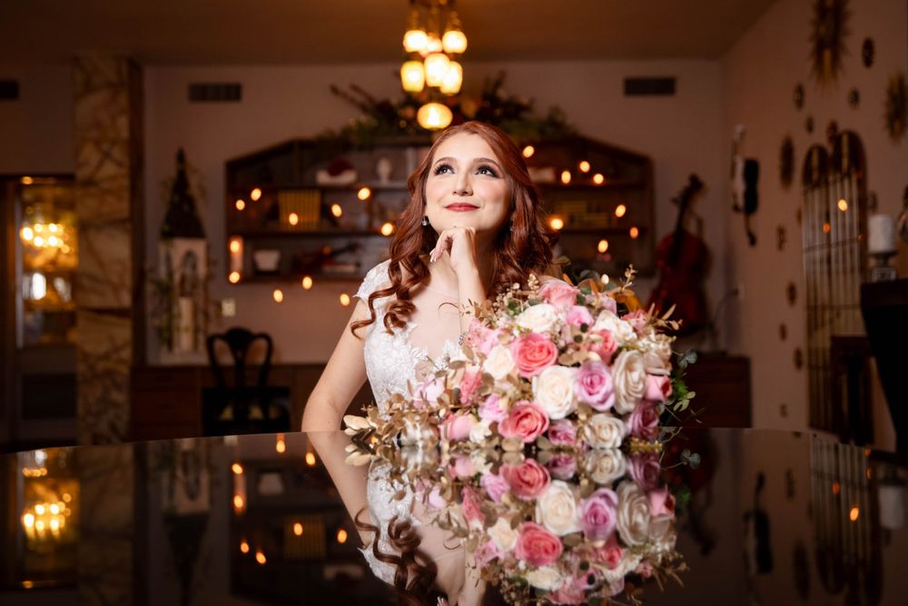 A person poses in an elegant venue holding a large pink and white floral bouquet with twinkling lights in background.