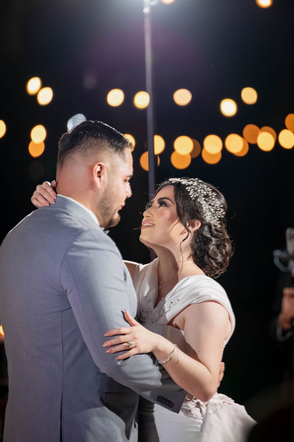 Couple shares intimate dance moment under string lights at outdoor wedding reception.