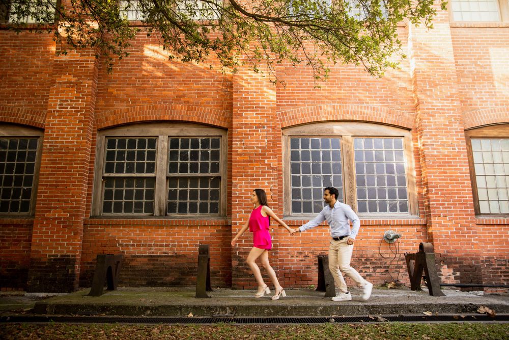 A playful couple dances outside a historic red brick building with arched windows.