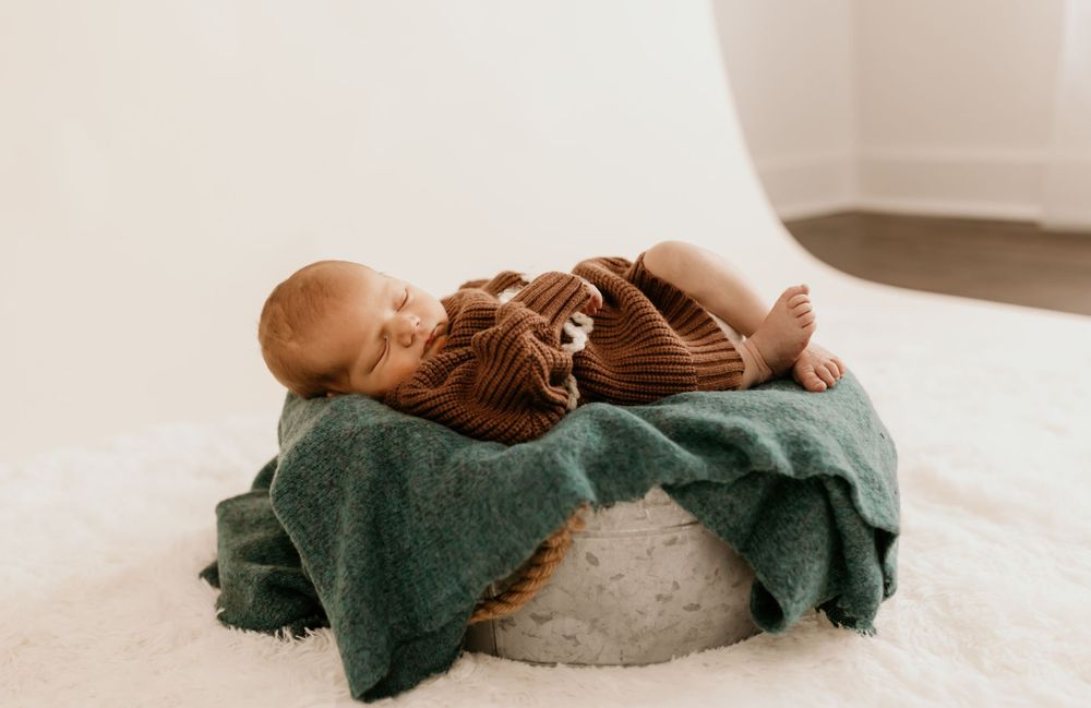 Peaceful newborn sleeping on a green blanket wearing a brown knitted outfit.
