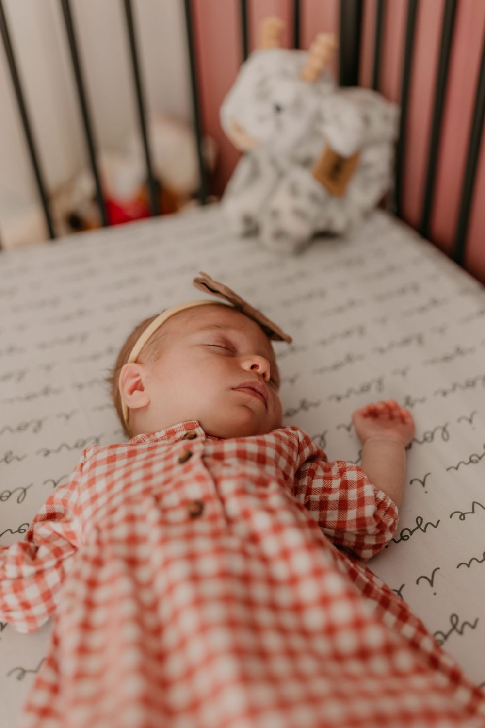 Sleeping baby in red gingham outfit rests peacefully in crib.