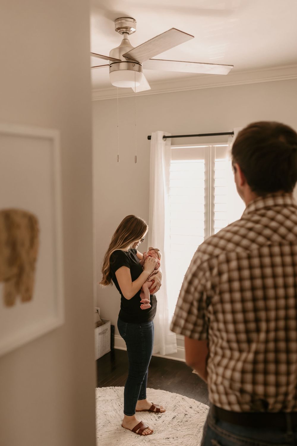 Parent holds infant while standing in sunlit nursery room.