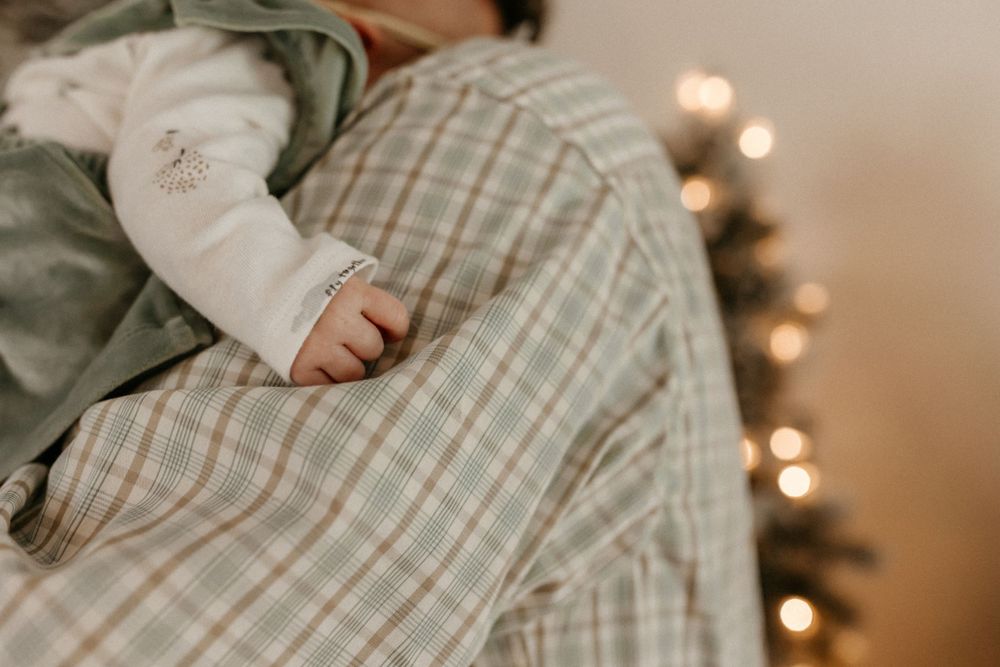 Small hand grasps plaid fabric with twinkling lights in background.