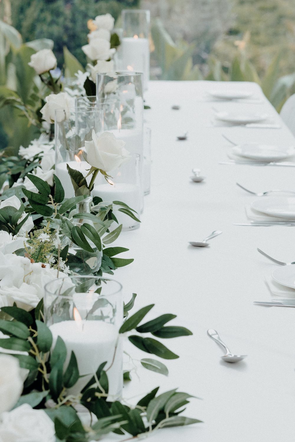 An elegant white wedding table setting with greenery garland, and candles captured by Apertured Media Auckland Wedding Photographer.