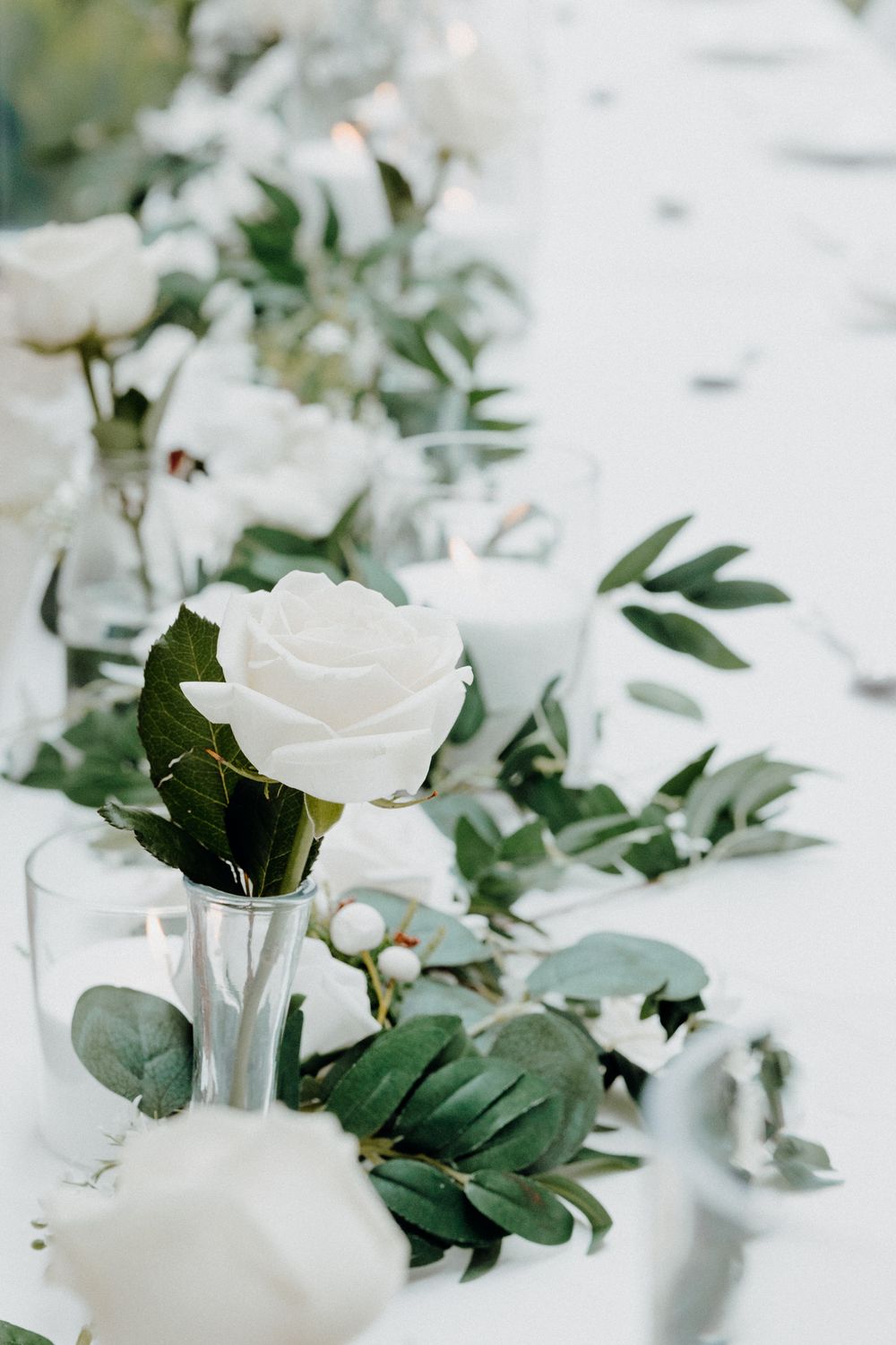 Delicate white roses and greenery arranged in glass vases captured by Apertured Media Auckland Wedding Photographer.