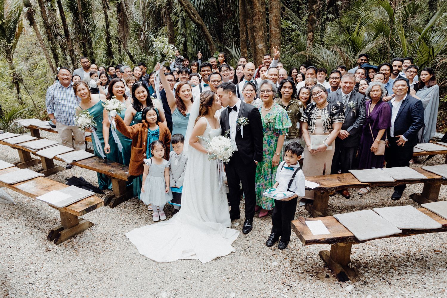 Wedding guests gather on rustic wooden benches for an outdoor forest ceremony captured by Apertured Media Auckland Wedding Photographer.