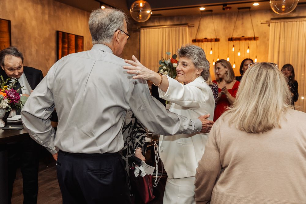 Wedding guests dancing and celebrating at an indoor reception with warm lighting.