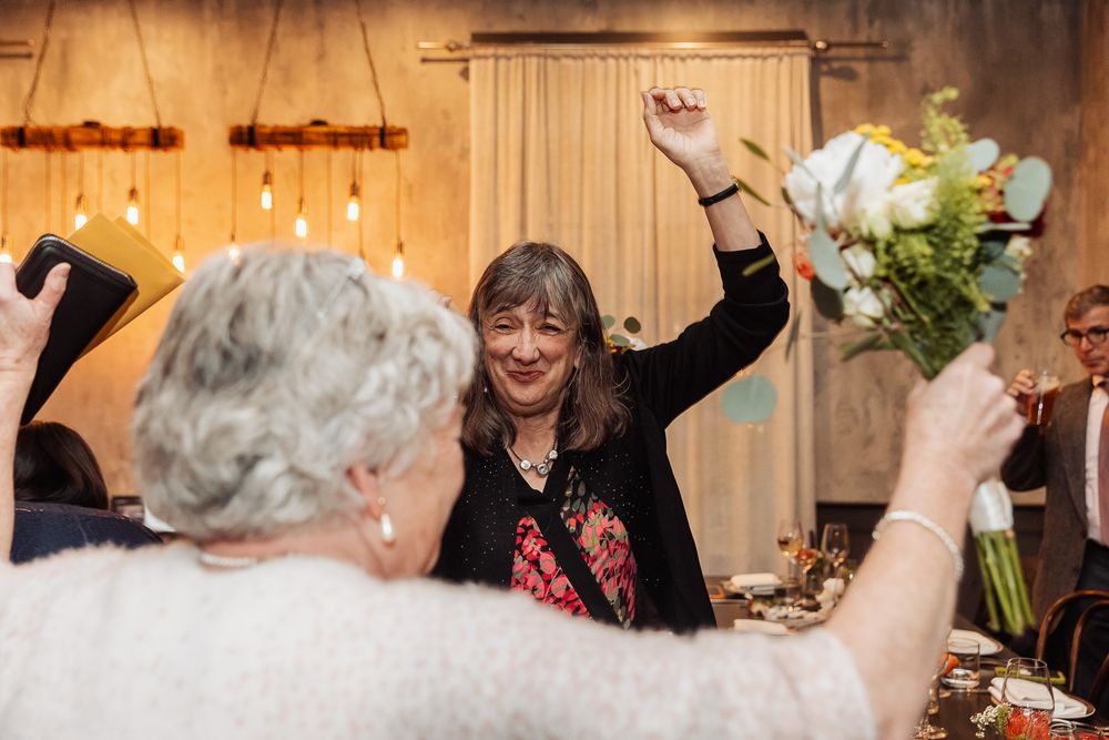 Two guests celebrating joyfully at an indoor celebration with raised arms and flowers.