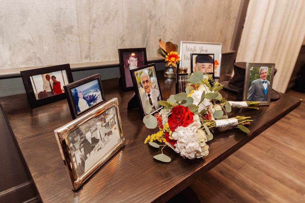 Memorial display with framed photos and floral arrangements on a dark wooden table.