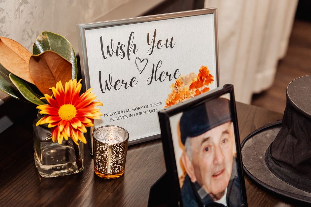 'Wish You Were Here' sign with orange flower and memorial photo on wooden table.