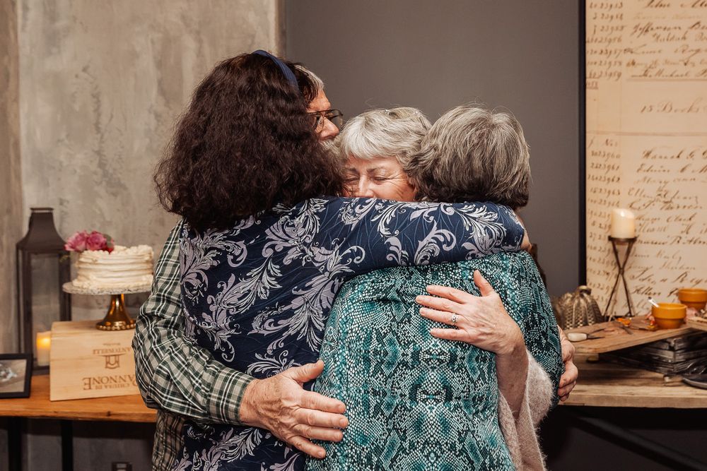 Emotional group hug between guests at indoor celebration.