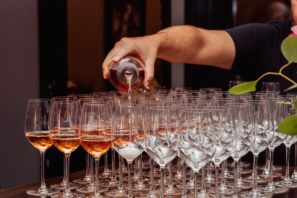 Hand pouring wine into multiple glass flutes at an event.