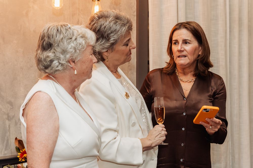 Three people engaged in conversation while holding drinks at an indoor gathering.