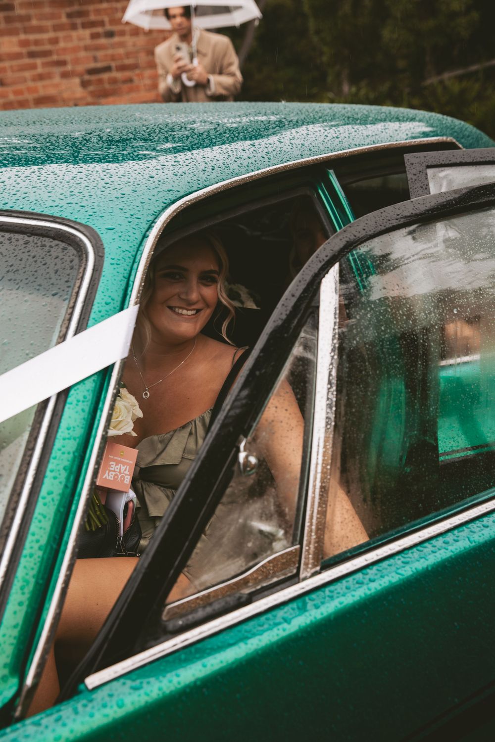 Wedding transportation in a vintage teal car on a rainy day.