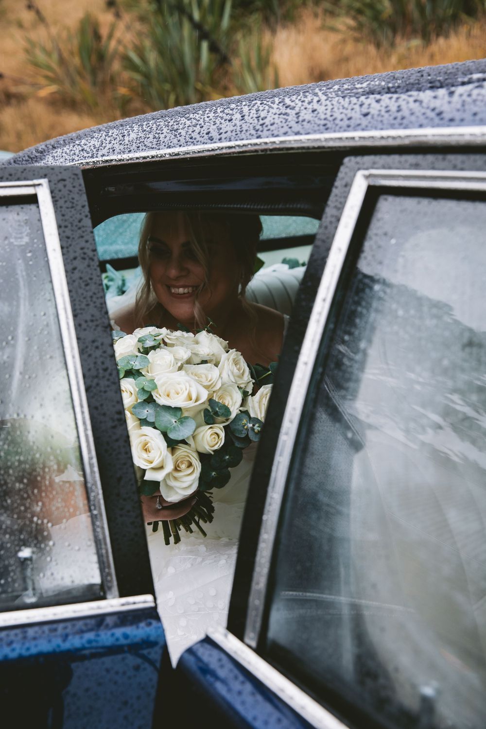 White rose bouquet viewed through car window on rainy day.