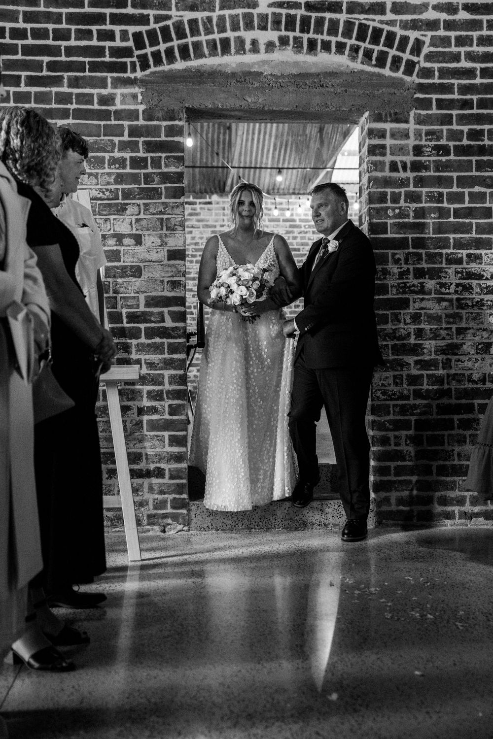 A couple stands framed in a brick archway during their wedding ceremony.