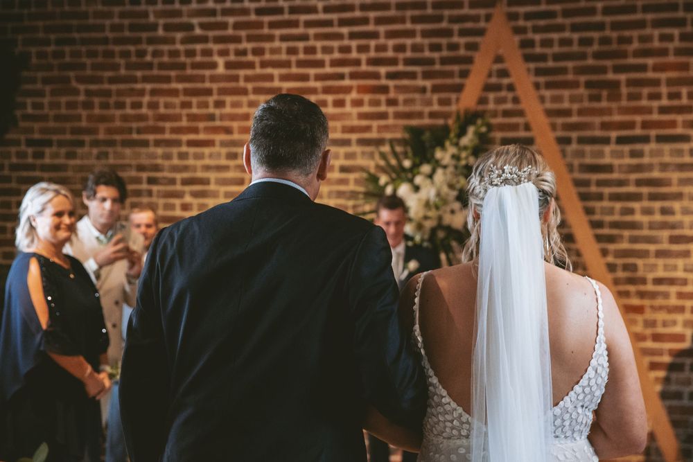 A wedding ceremony takes place in front of a triangular arch against exposed brick walls.